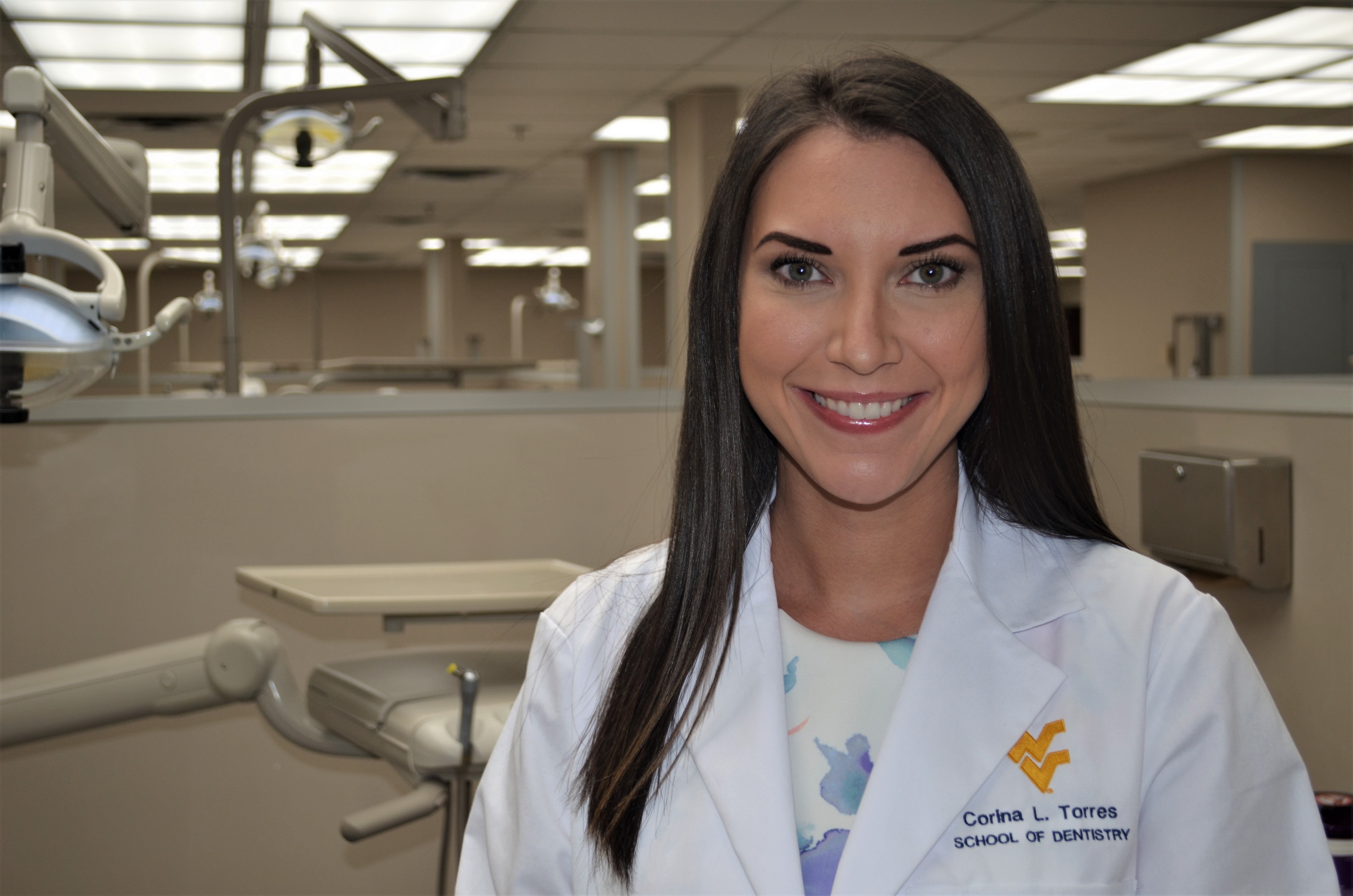 Corina Torres poses in her white coat in the School of Dentistry main student clinic. 